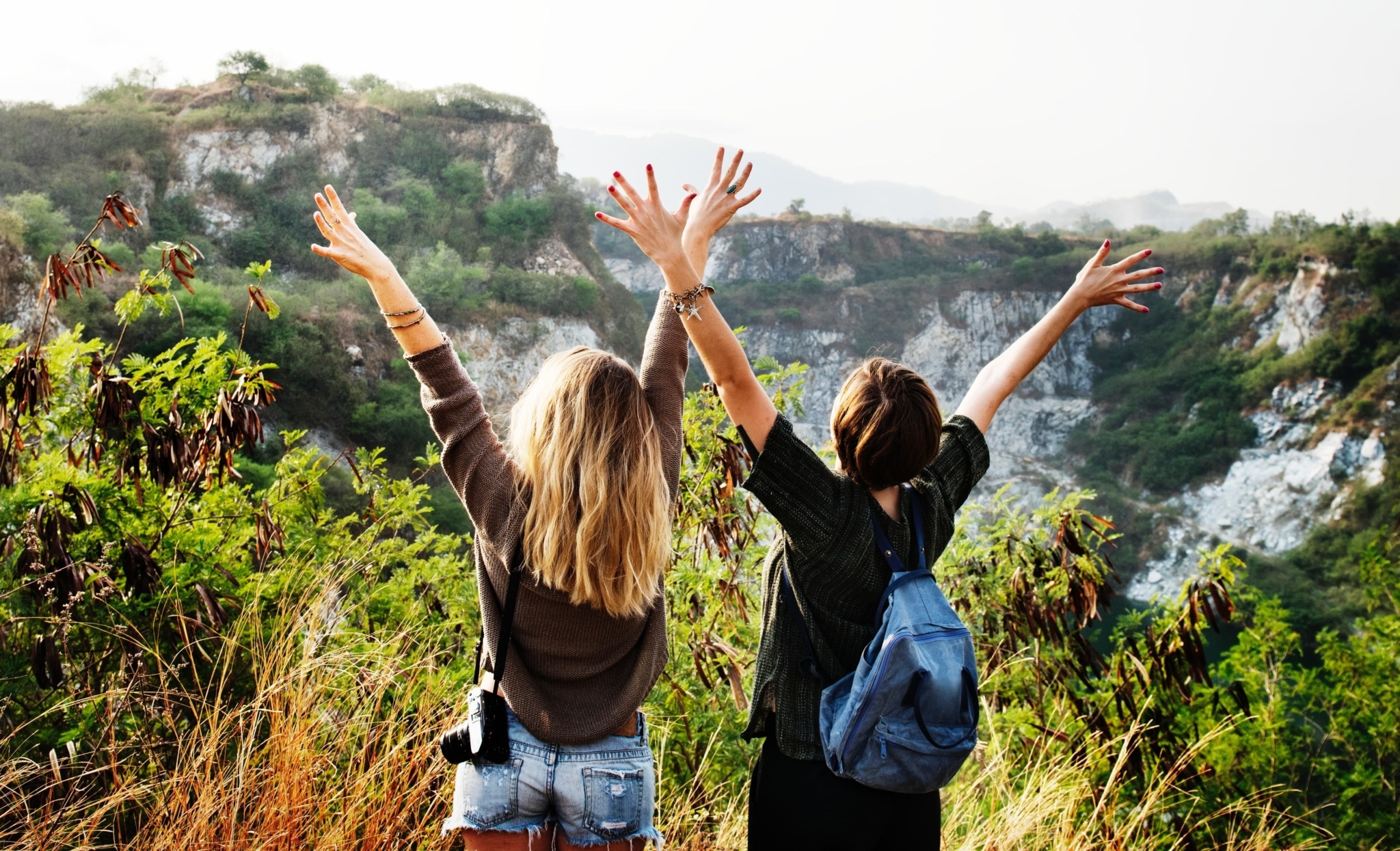 Two person raising their hands facing mountain